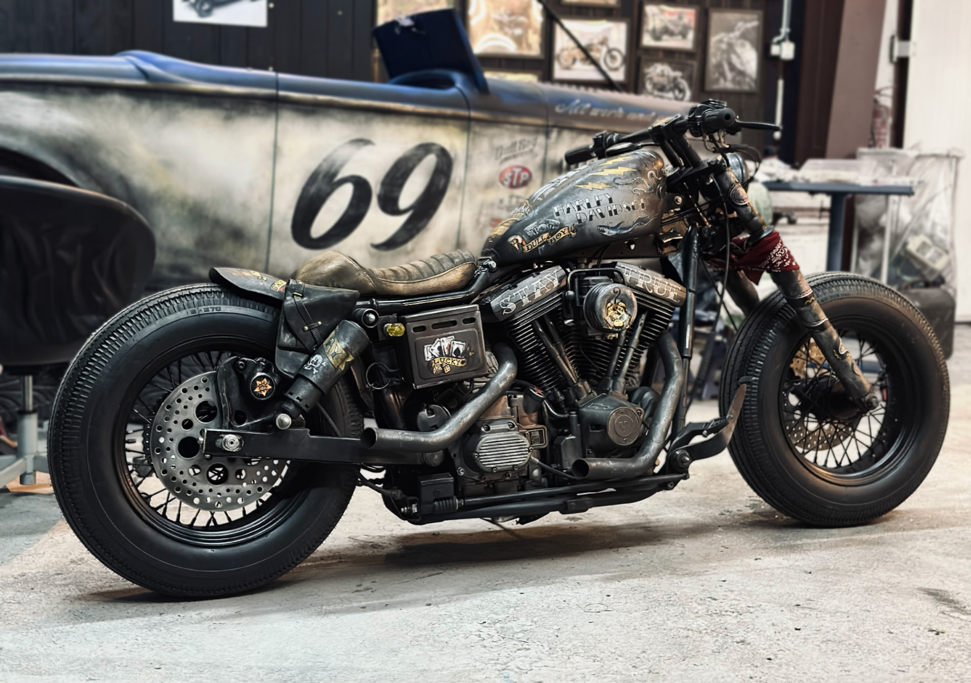 Custom Harley-Davidson bobber with hand-painted graphics and vintage race car number 69 in background