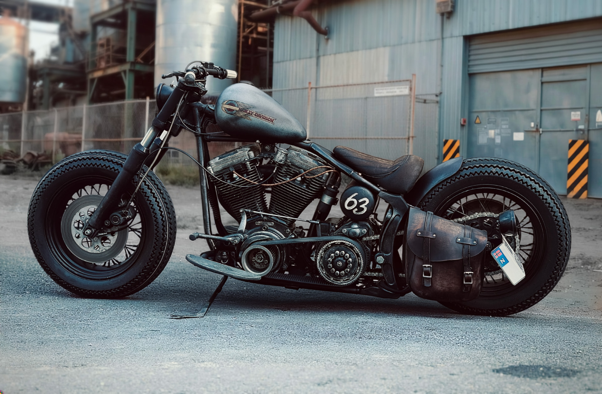Custom Harley-Davidson bobber with number 63 side panel and leather saddlebag in an industrial yard